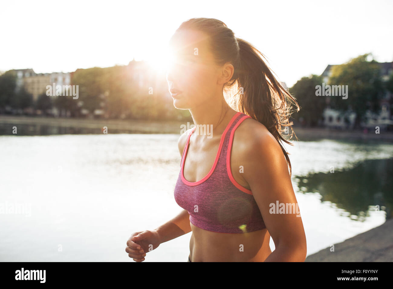Colpo all'aperto di determinata giovane donna fuori per una corsa nel parco della città. Sportive jogging in un giorno di estate con sun flare. Foto Stock