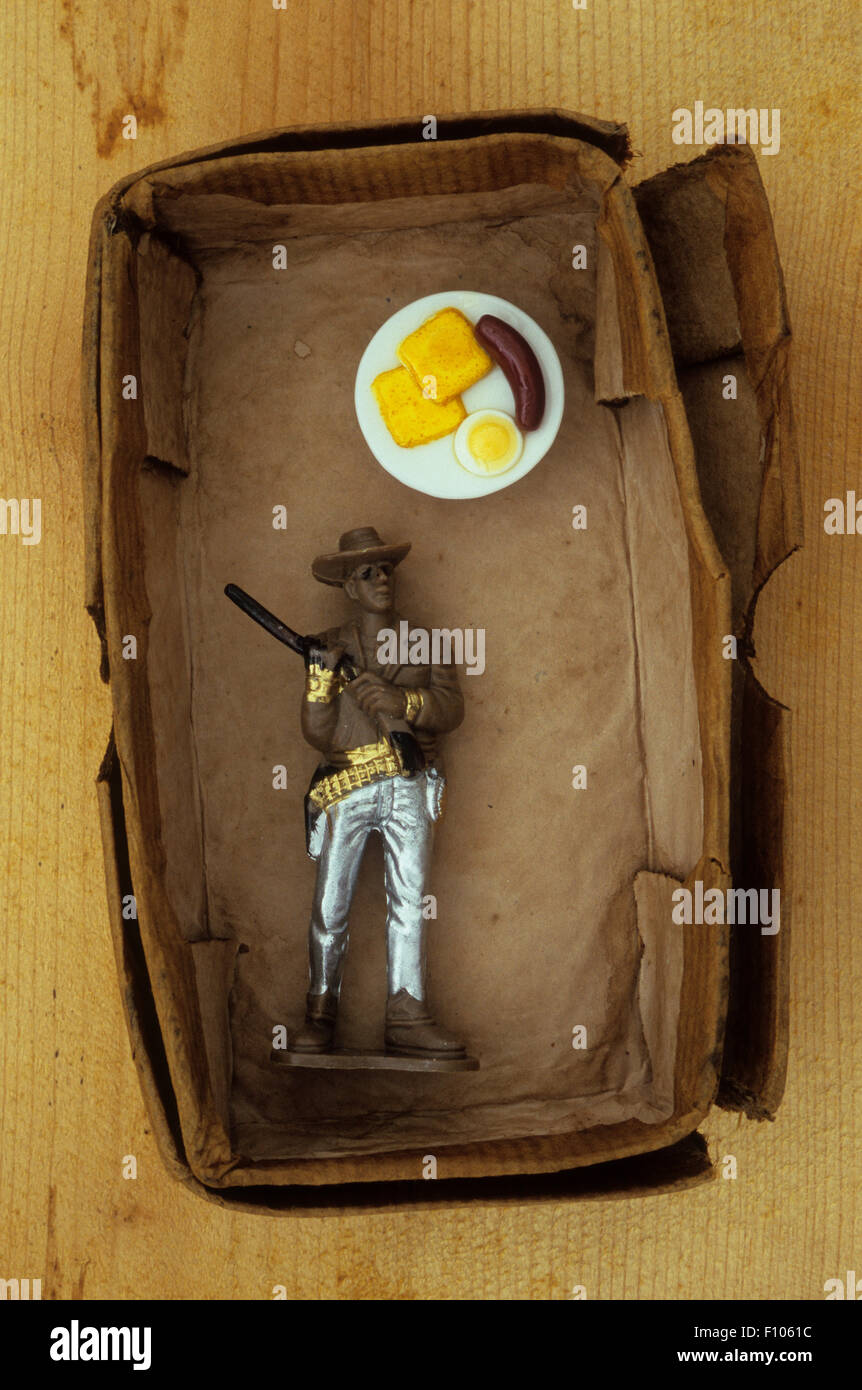 Modello di plastica del cowboy holding fucile sulla spalla e fantasticando su piastra colazione di salsicce e uova Foto Stock