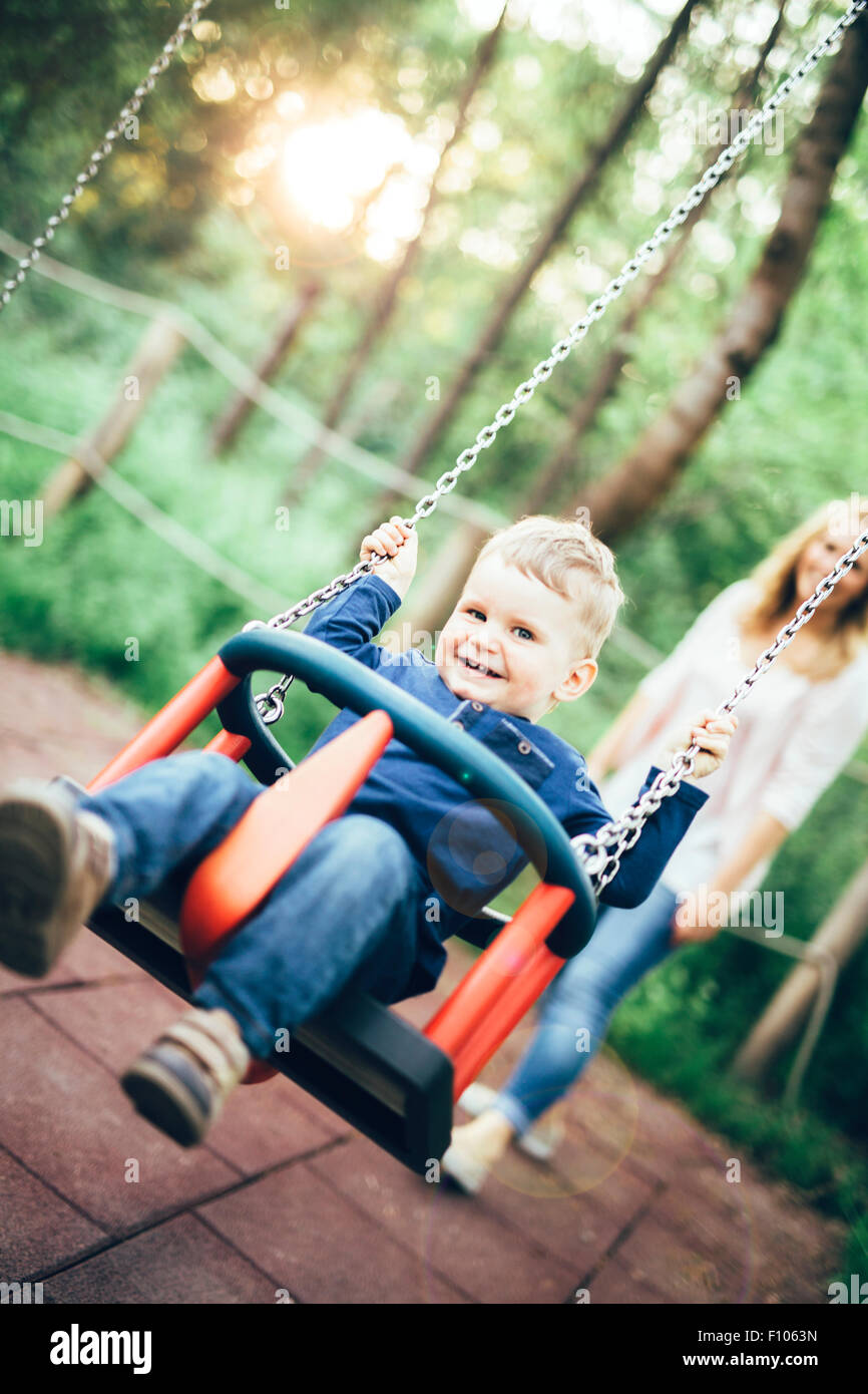 La madre e il bambino all'aperto nel parco giochi a cavallo di un swing e sorridente Foto Stock