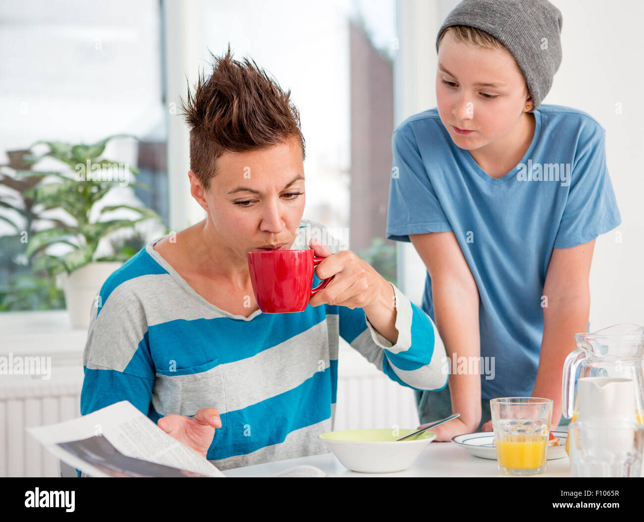 Madre e figlio avente la quale include la prima colazione al mattino. La madre sta leggendo il giornale e il figlio è guardare oltre la sua shoulde Foto Stock