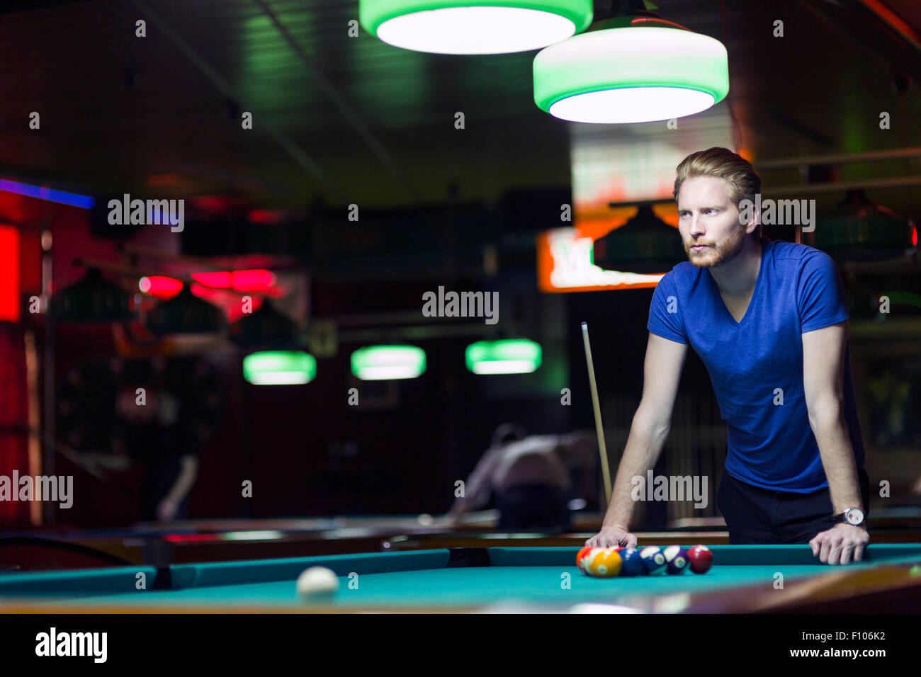 Bel giovane giocatore di snooker la piegatura sopra la tavola in un bar con una bella illuminazione ambientale Foto Stock