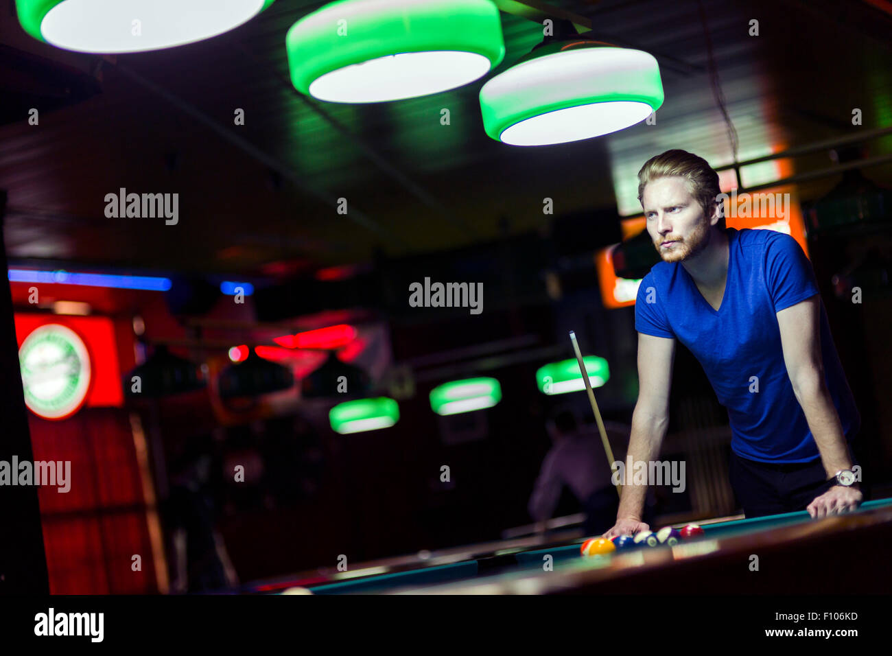 Bel giovane giocatore di snooker la piegatura sopra la tavola in un bar con una bella illuminazione ambientale Foto Stock