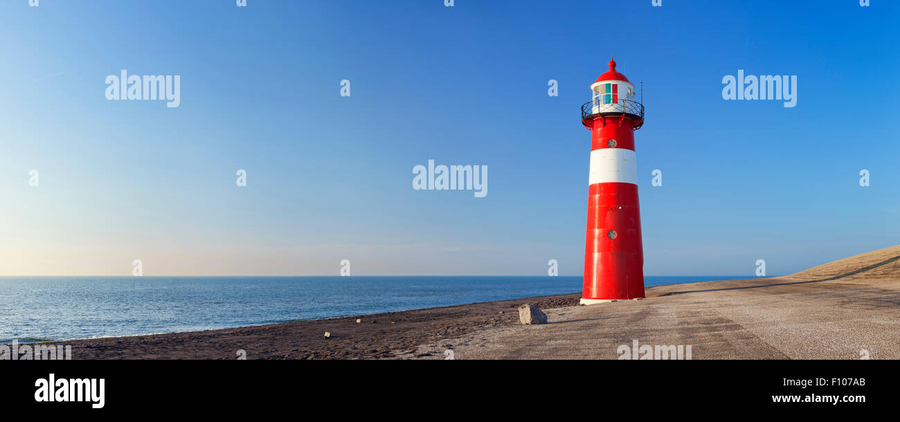 Un rosso e bianco faro di mare sotto un cielo blu chiaro. Fotografato vicino a Westkapelle in Zeeland, Paesi Bassi. Foto Stock