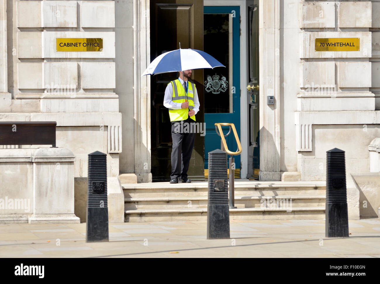 Londra, Inghilterra, Regno Unito. La guardia di sicurezza al di fuori del Cabinet Office, 70 Whitehall, tenendo un ombrello in una giornata di sole nel mese di agosto Foto Stock