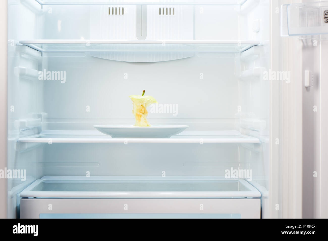 Apple core sulla piastra bianca in aprire il frigorifero vuoto. Perdita di peso la dieta concetto. Foto Stock