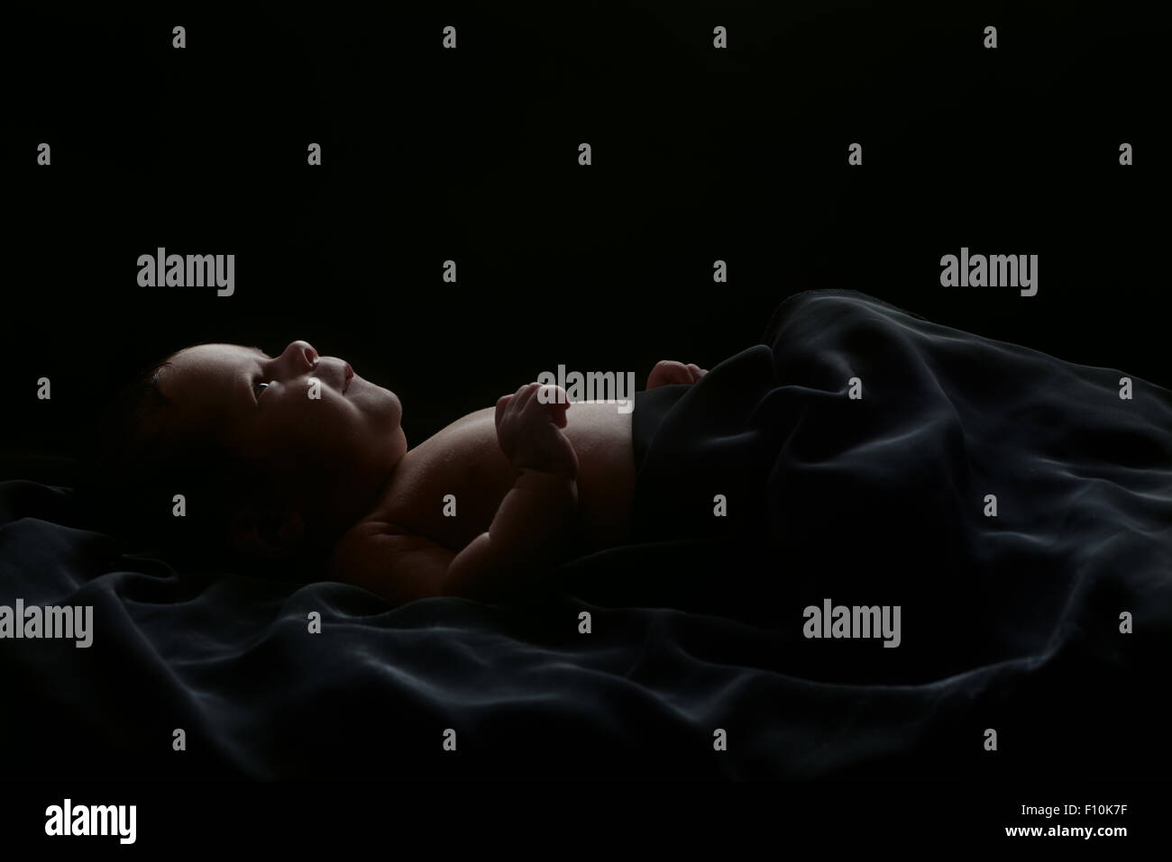 Carino neonato shot in studio giacente, coperto con soffice coltre nera, isolato su sfondo nero Foto Stock