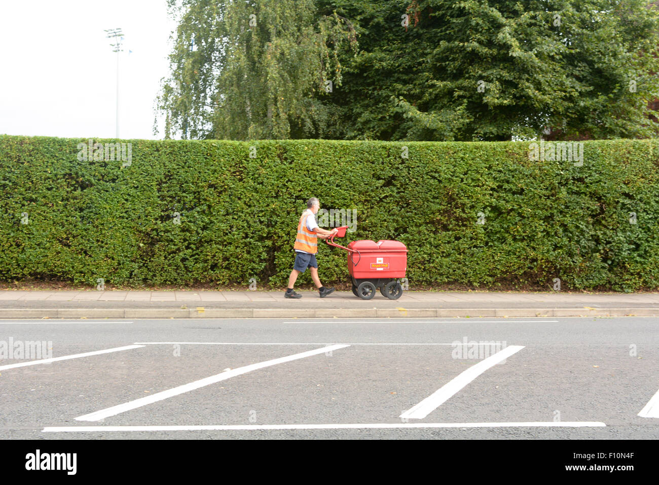 Portalettere con Royal Mail spingere il carrello facendo postale sulla rotonda Goldington Road in Bedford Bedfordshire Inghilterra Foto Stock