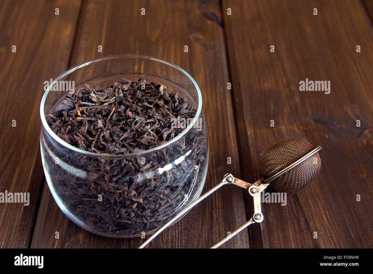 Black dry le foglie di tè in un barattolo di vetro su sfondo di legno Foto Stock