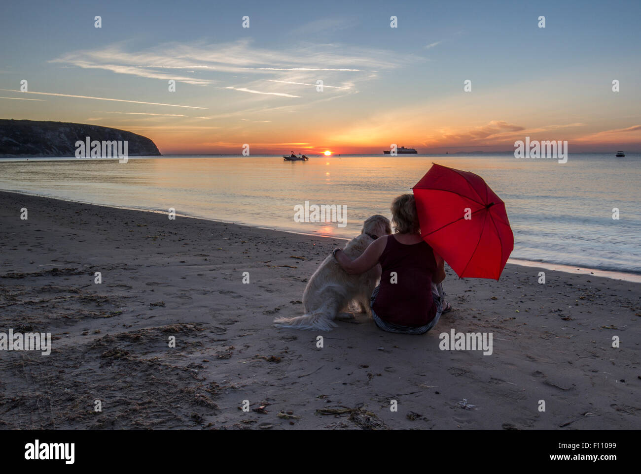 Il pet retriever e donna con ombrello rosso godendo il sunrise in Swanage Bay Foto Stock