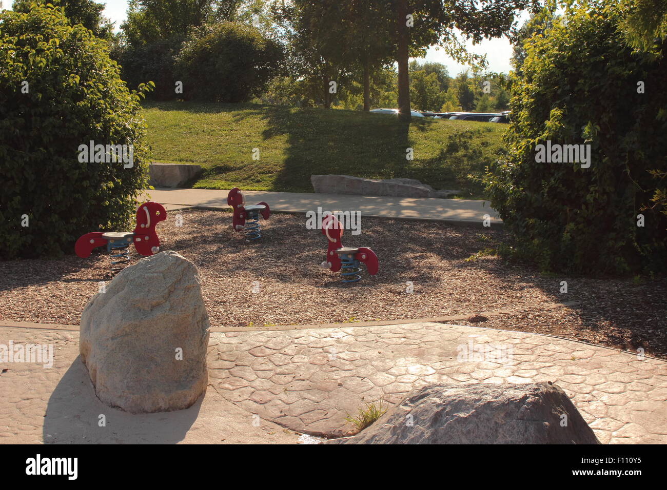 Tre sedili liberi, tre rossi cavalli a dondolo con bobina primavera presso un pubblico parco della città a nord di Indianapolis, centrato, molta ombra Foto Stock