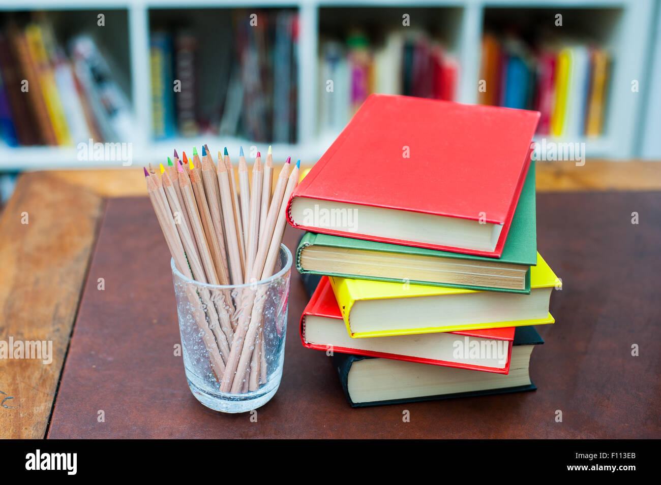 Matite colorate in vetro porta penna con la pila di libri con vari colori copre Foto Stock