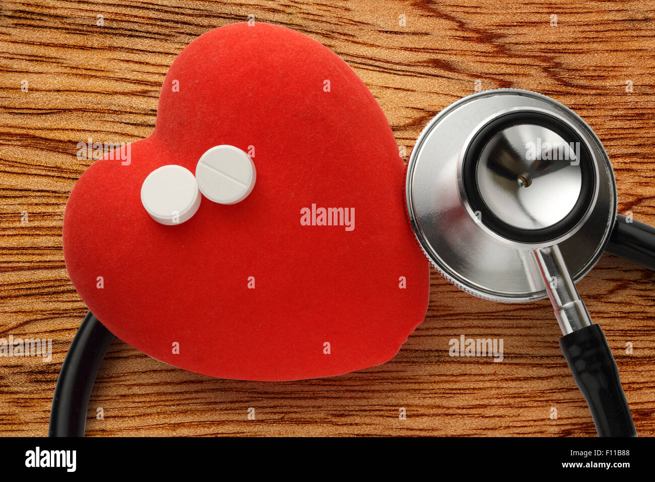 Cuore rosso, uno stetoscopio e pillole su sfondo di legno Foto Stock
