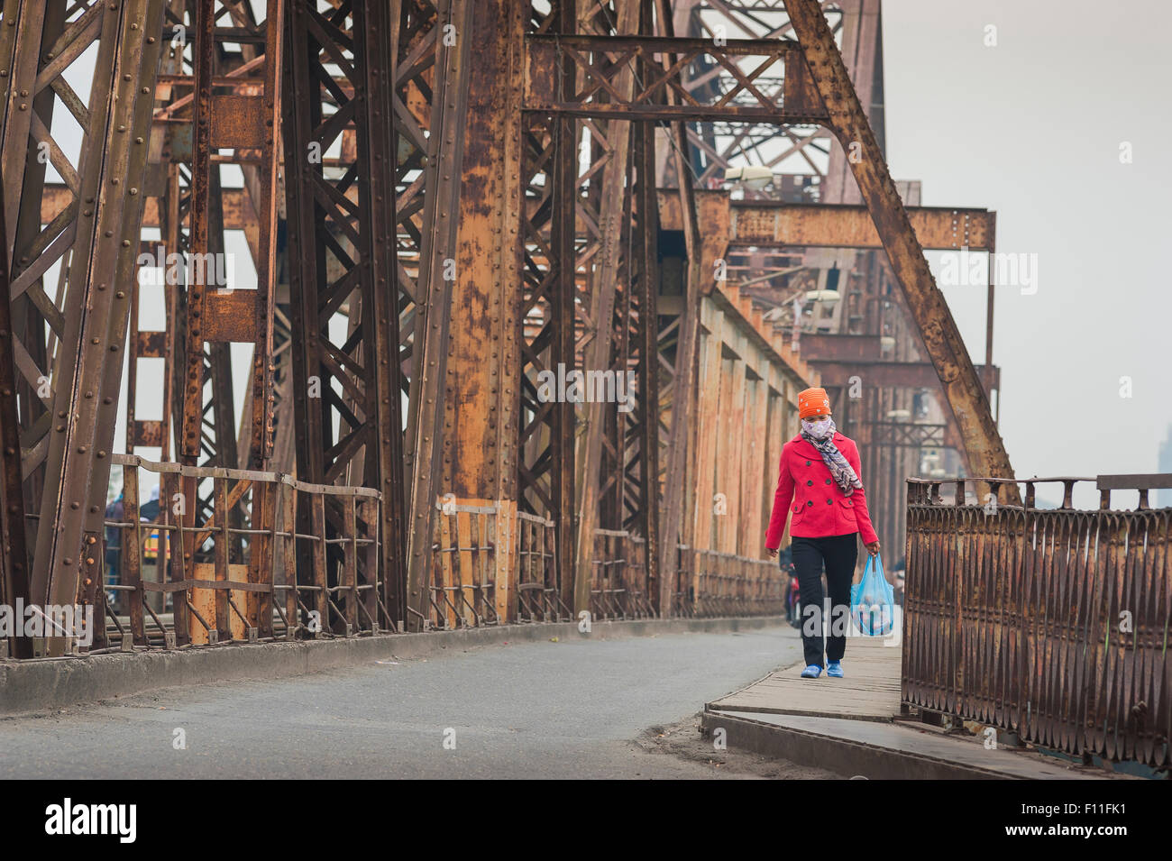 Donna che cammina da sola, veduta di una giovane donna vietnamita che indossa una maschera facciale che cammina attraverso il Long Bien Bridge in una giornata coperta e fumosa, Hanoi Vietnam Foto Stock