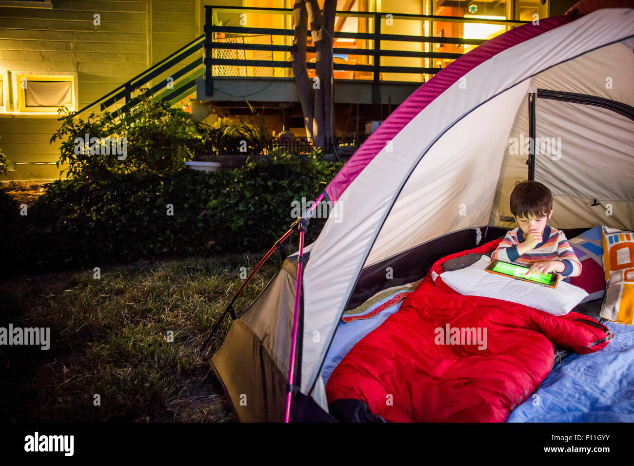 Razza mista boy utilizzando digitale compressa nella tenda del cortile Foto Stock