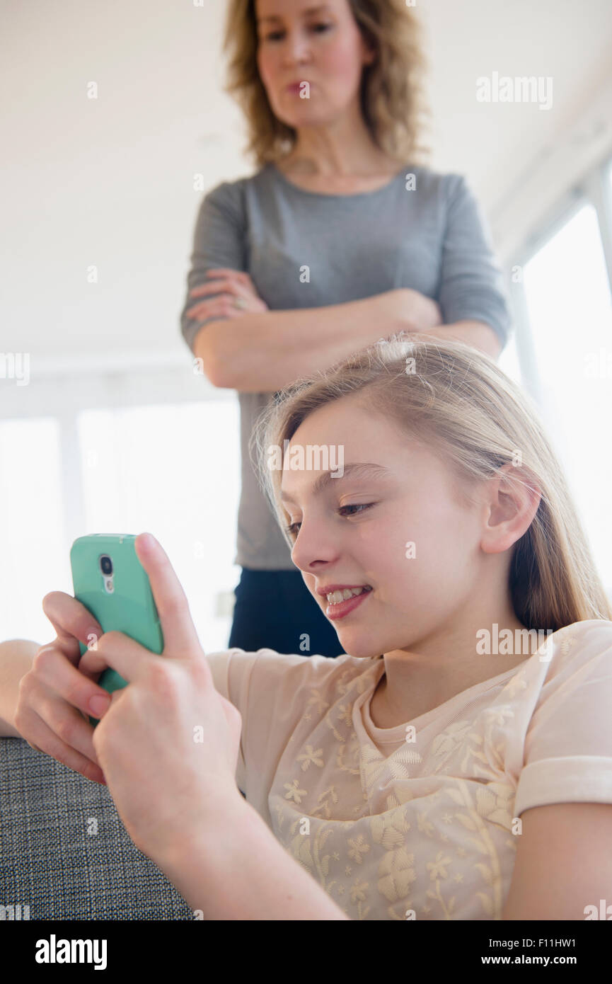 Madre caucasica guardando la figlia uso telefono cellulare Foto Stock