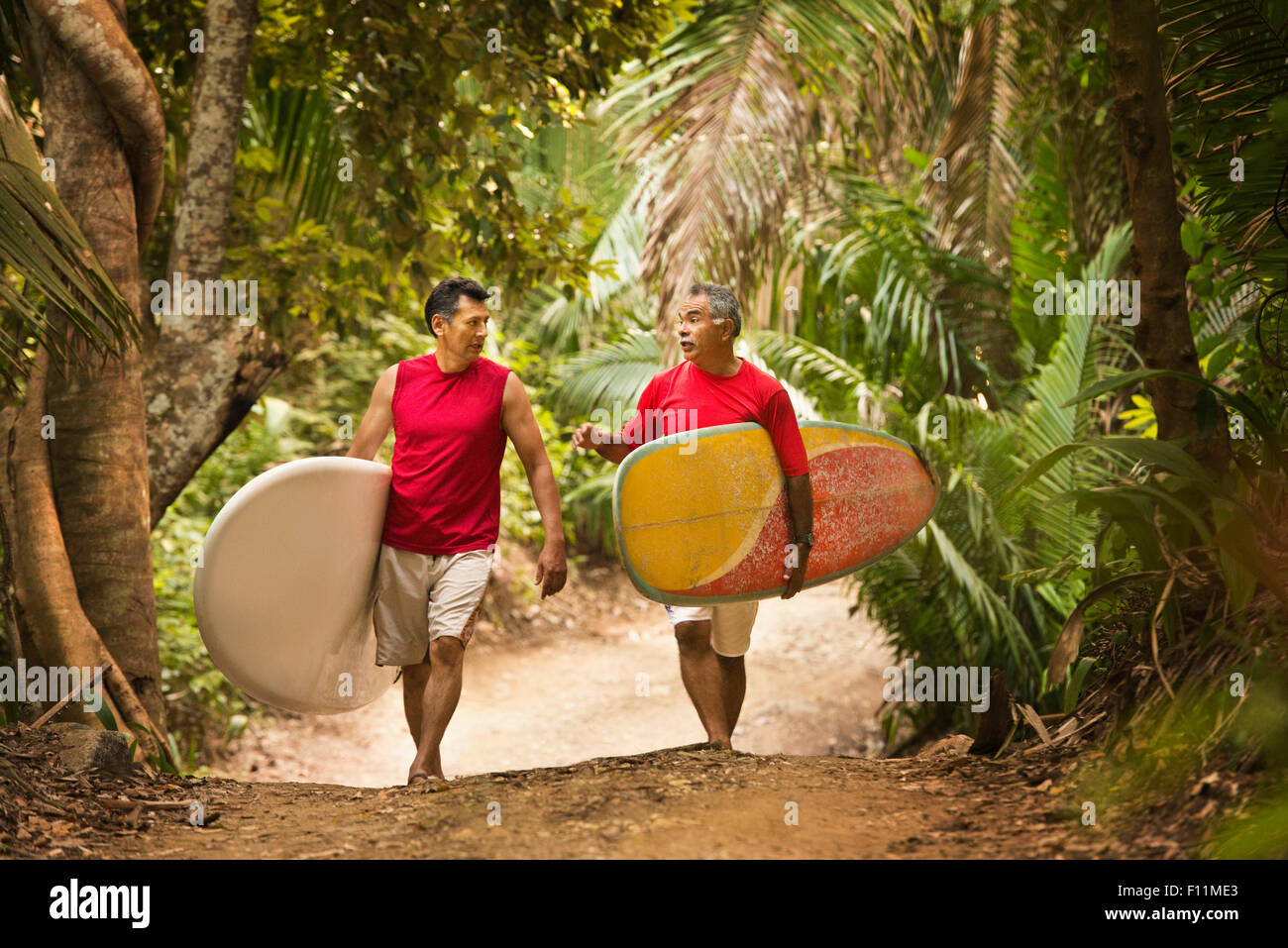 Ispanico gli uomini che trasportano le tavole da surf sul sentiero nella giungla Foto Stock
