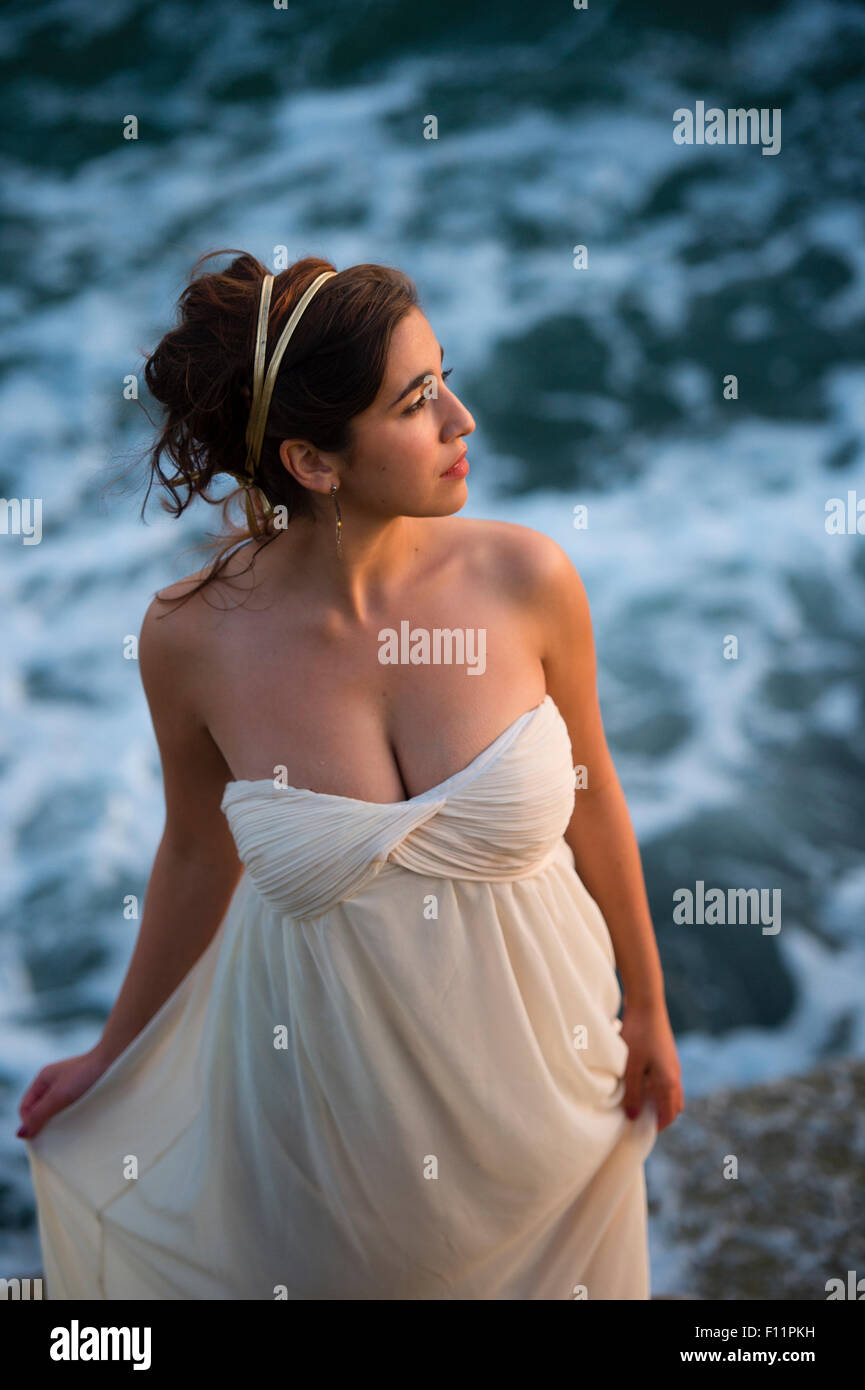 Un grazioso scuoiate di oliva dai capelli scuri donne ragazza di modellazione in posa come un "dea greca' in piedi sull'oceano Foto Stock