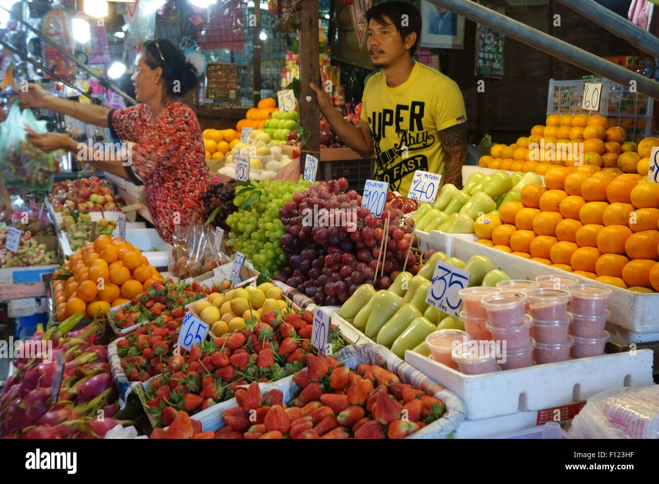 Pressione di stallo di frutta in una Bangkok mercato alimentare con prezzi in baht tailandese e una donna che serve i clienti, Thailandia Foto Stock