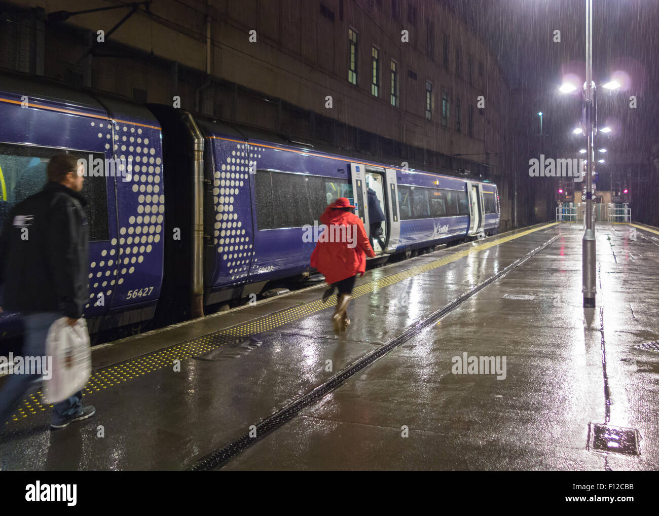 Woman in Red cappotto e hat correre per prendere il treno sotto la pioggia durante la notte Foto Stock