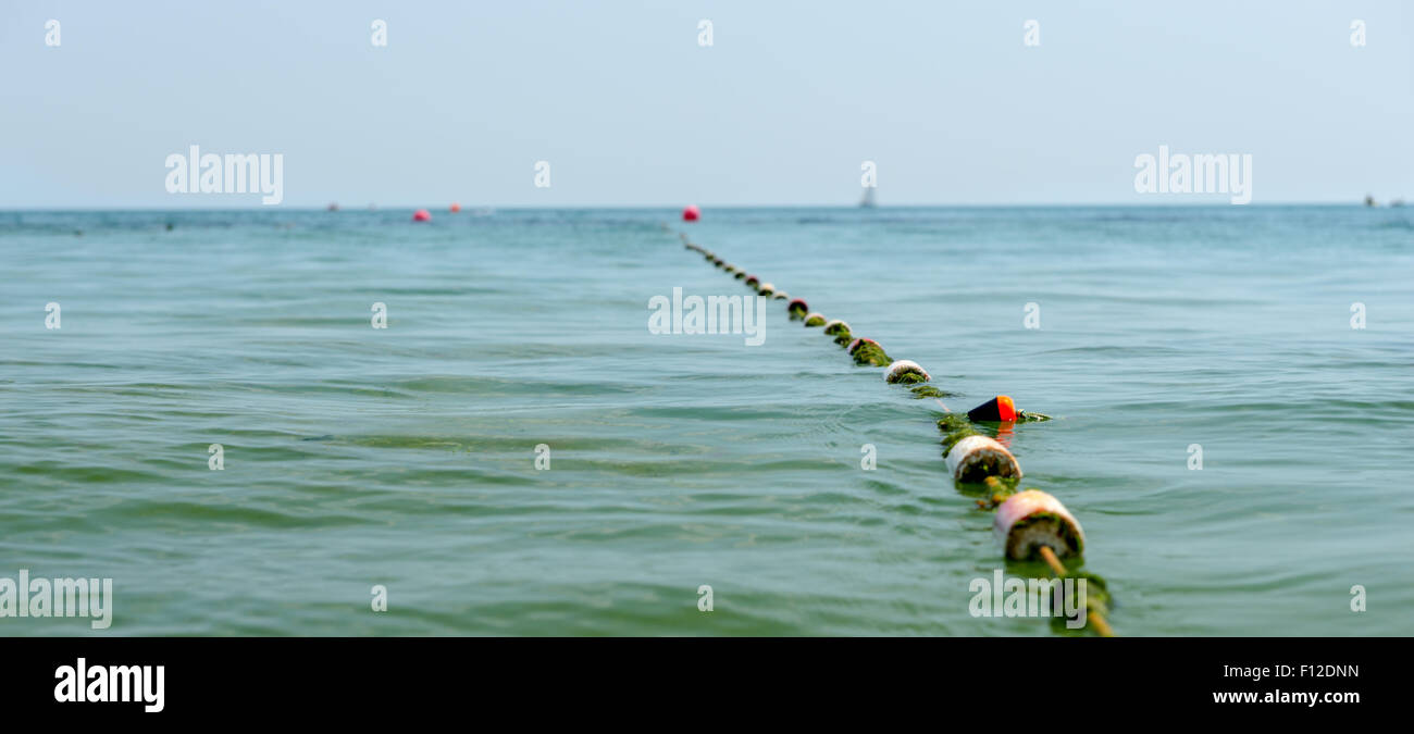 Fila di collegato galleggia sull'oceano la marcatura di un canale o di un ingresso di un marina o porto in un resort per vacanze attaccato ad una boa rosso in distanza. Foto Stock