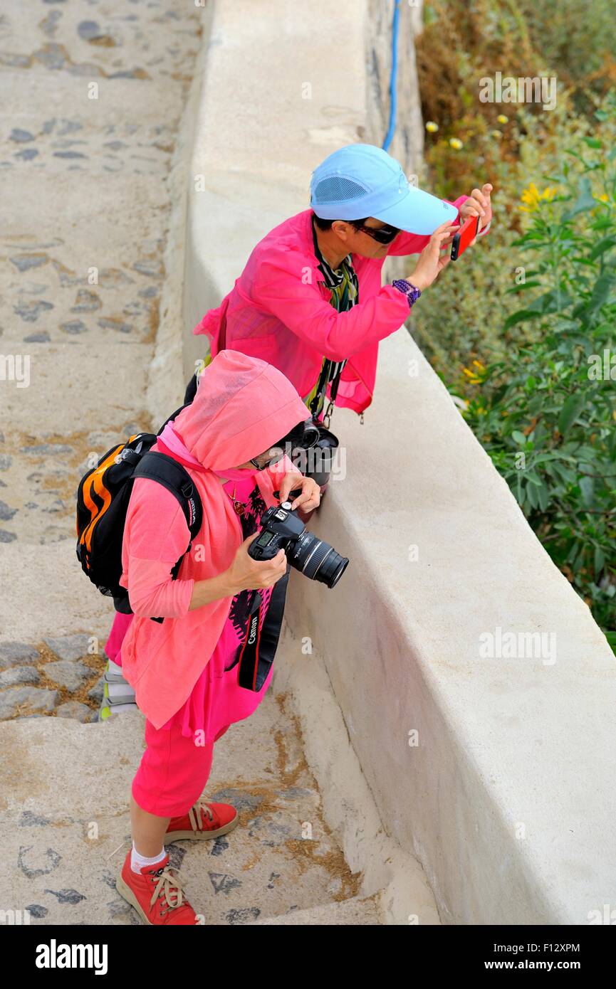 Due turisti asiatici vestito in rosa fotografare il paesaggio di Santorini Grecia Foto Stock