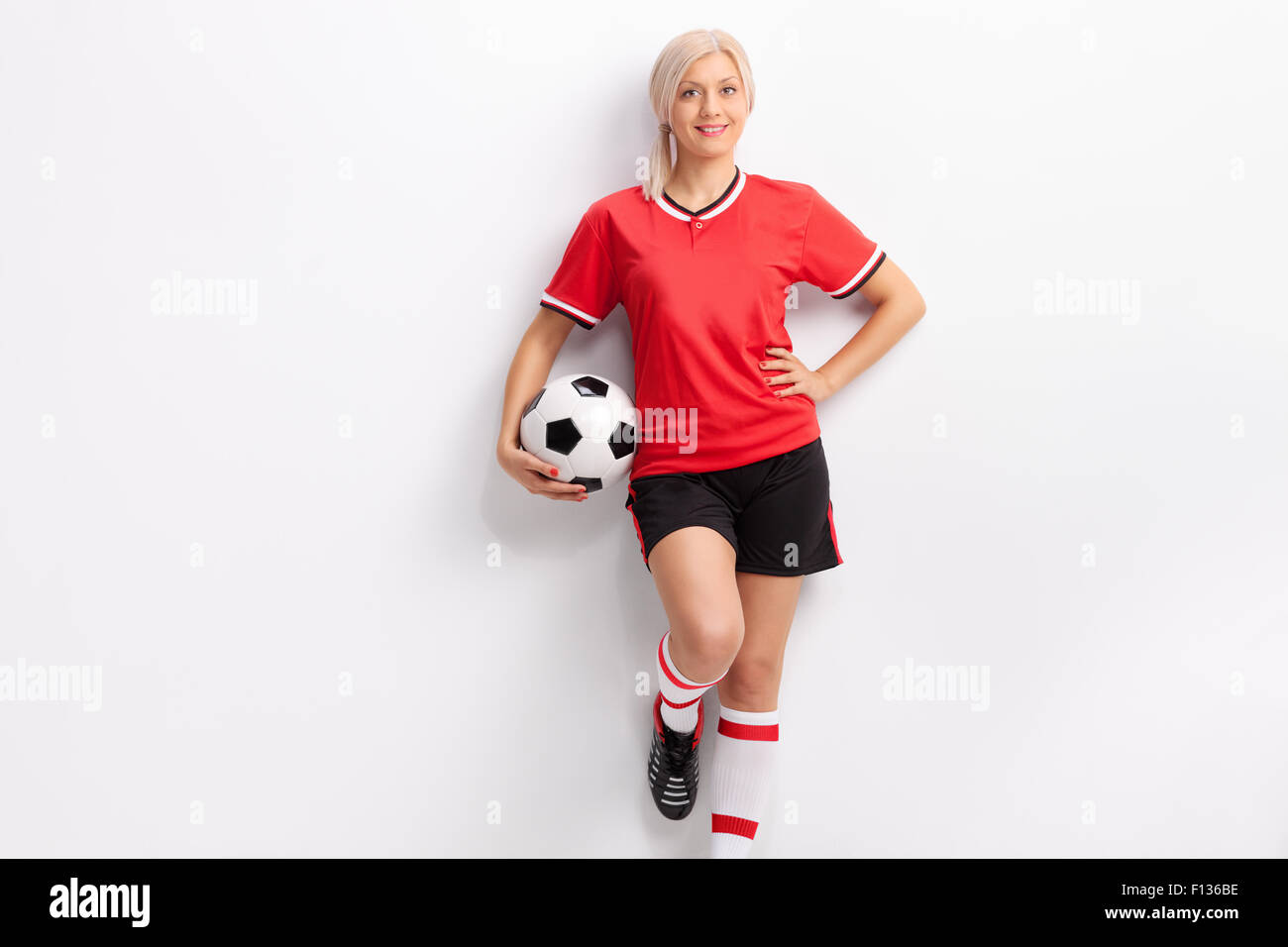 Femmina giocatore di calcio in una maglia rossa e pantaloncini neri tenendo  una palla e poggiante contro una parete Foto stock - Alamy