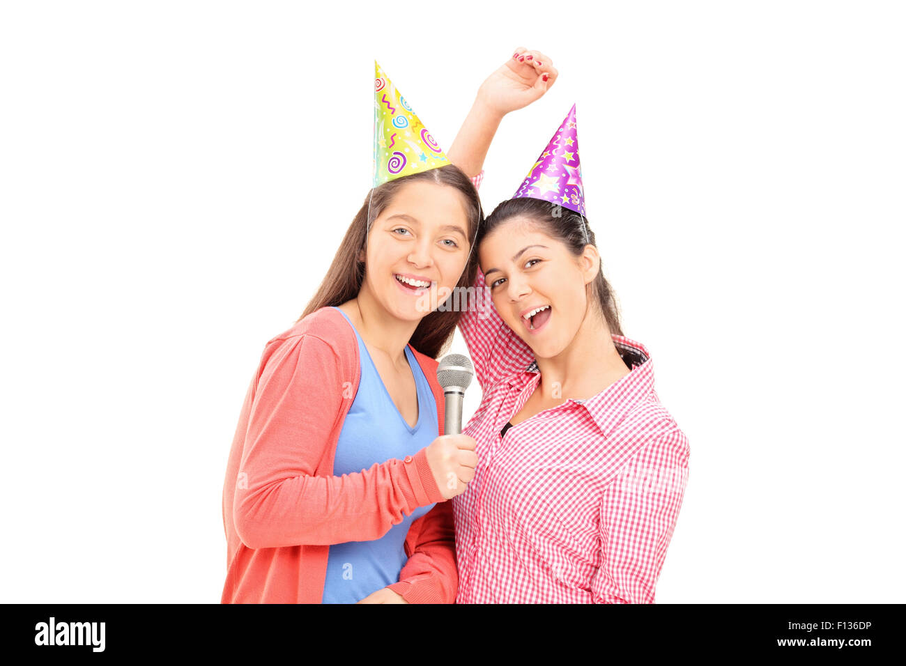 Due ragazze adolescenti con party cappelli cantando su un microfono e guardando la telecamera isolata su sfondo bianco Foto Stock