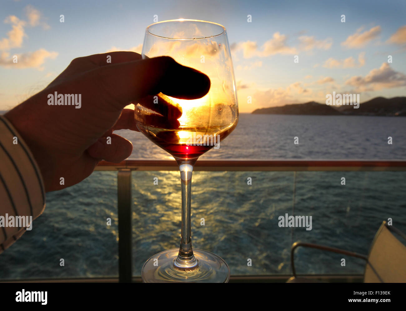 Titolare di una pensione o di una rendita in mano un bicchiere di vino guardando il tramonto dalla sua nave da crociera balcone Foto Stock