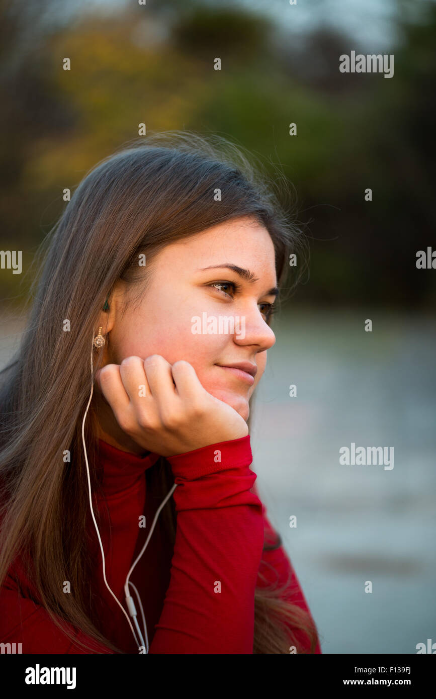 Giovane donna felice che ascolta la musica con le cuffie Park e indossa un pullover rosso Foto Stock