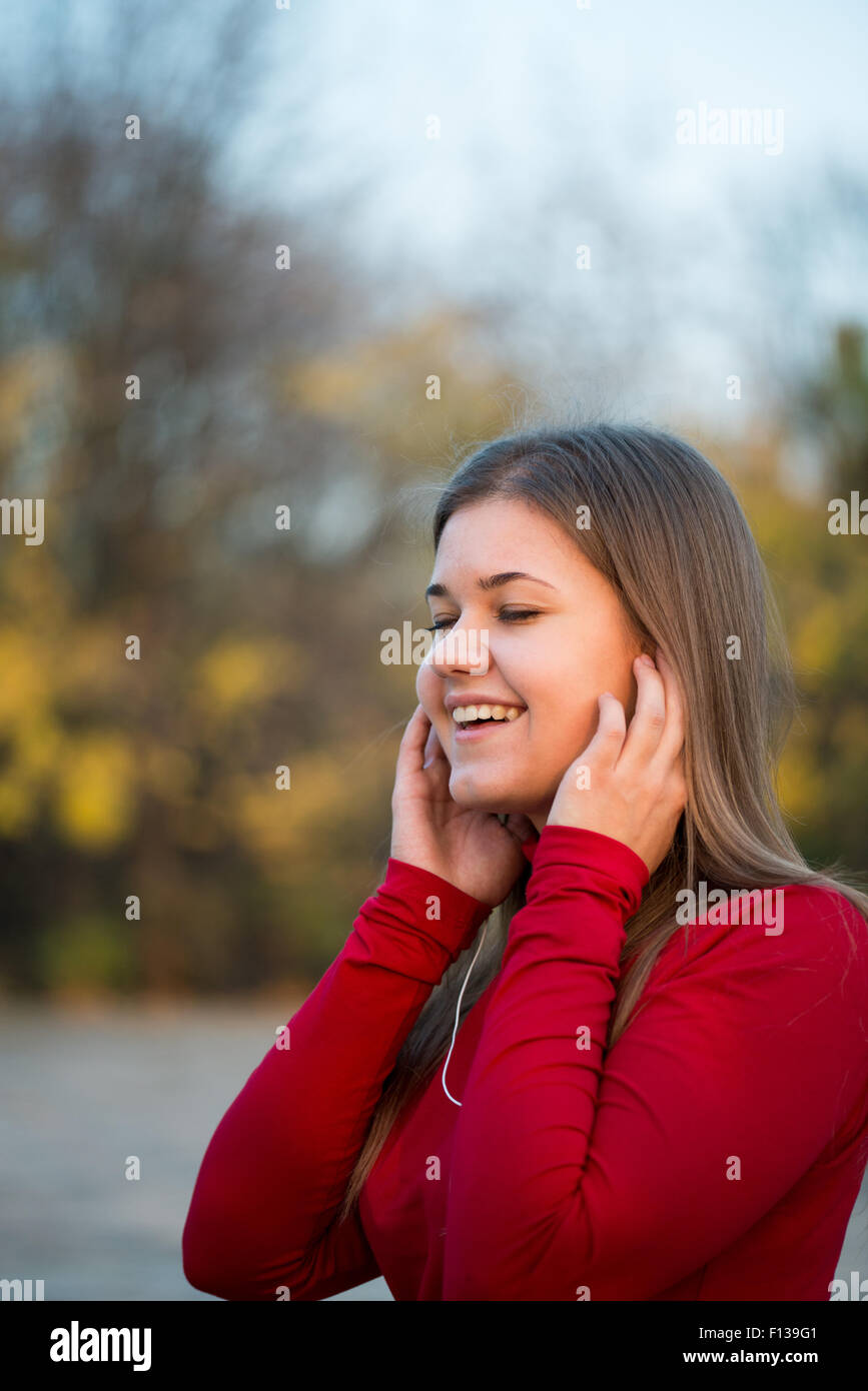 Giovane donna felice ascolto di musica con cuffie e cantare in autunno park, indossare pullover rosso Foto Stock