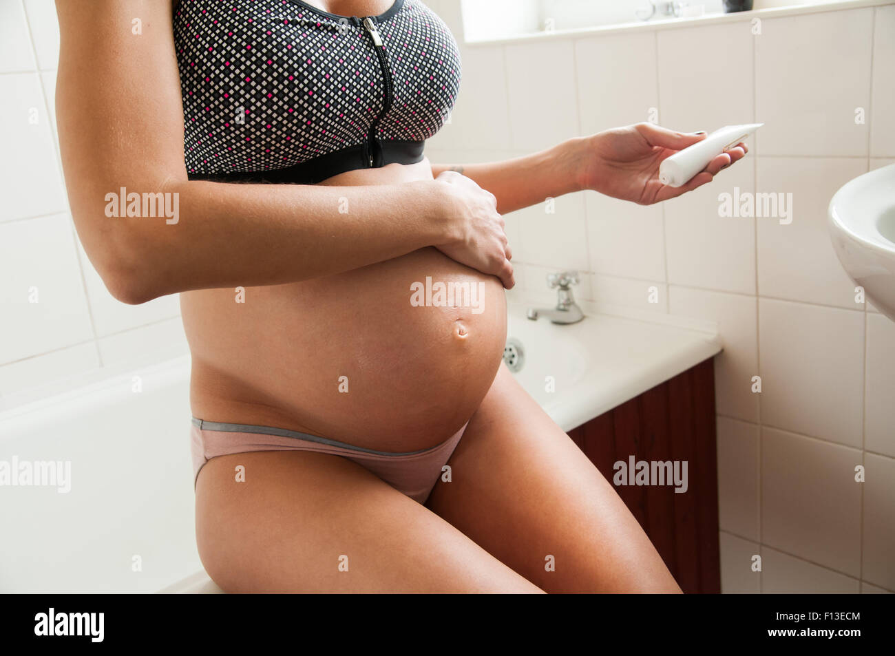 Donna incinta idratante di sfregamento sul suo ventre Foto Stock