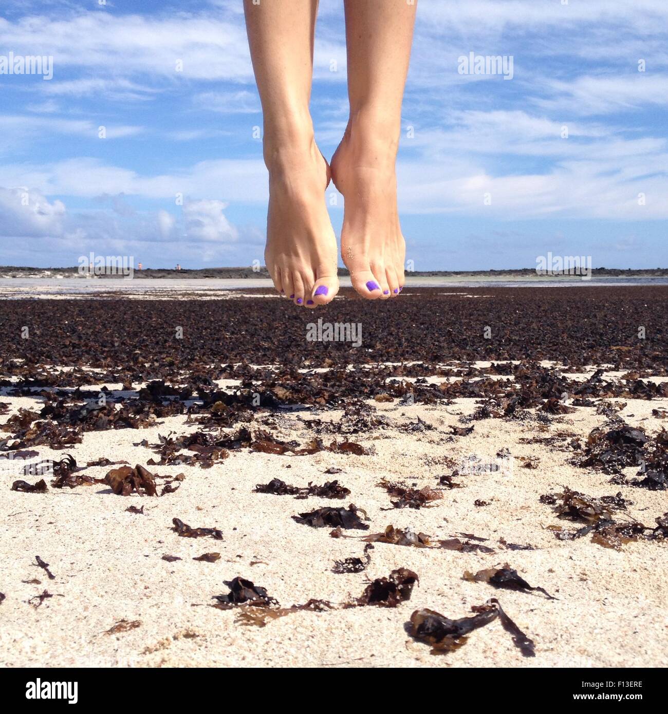 Donna che salta in aria sulla spiaggia Foto Stock