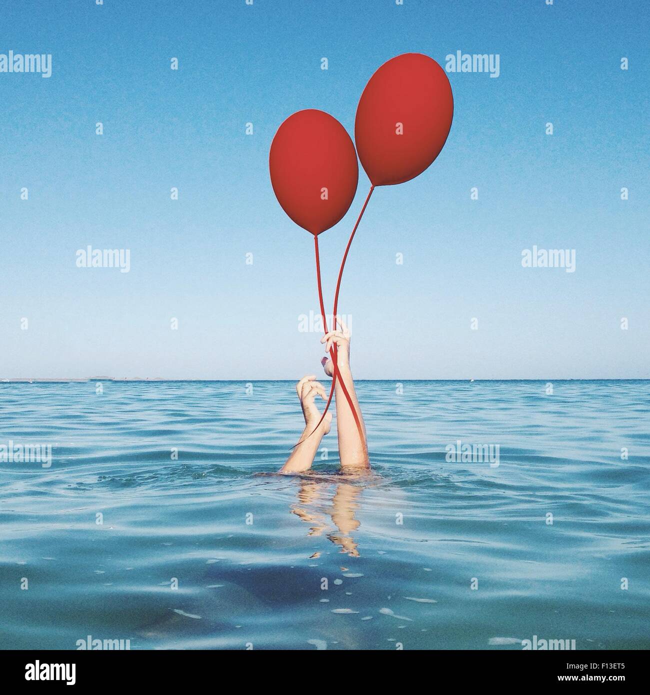 Le mani umane provenienti dal mare con due palloncini Foto Stock