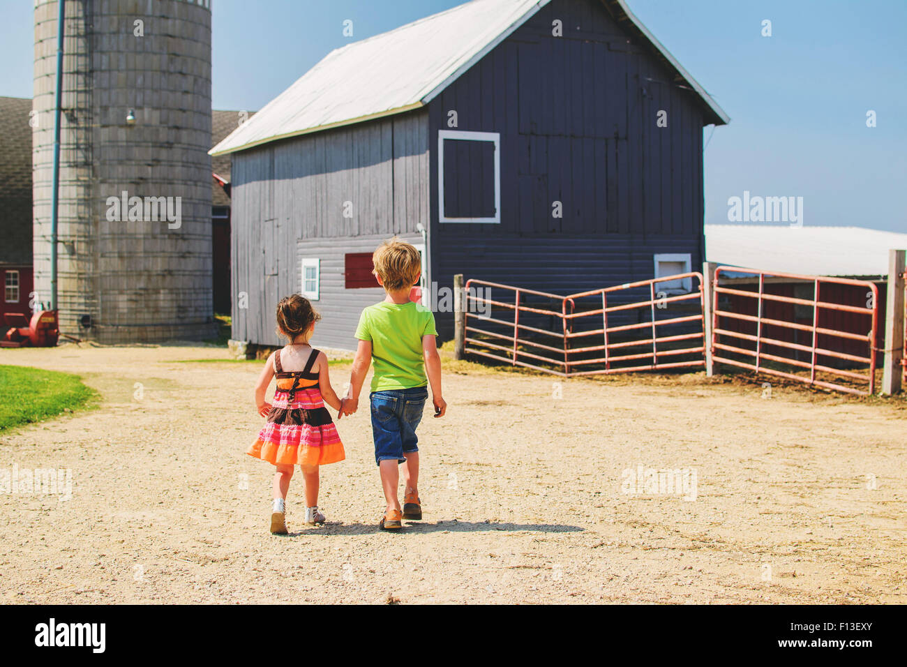 Vista posteriore di una ragazza e di un ragazzo che tengono le mani, camminando verso gli edifici agricoli, Stati Uniti Foto Stock