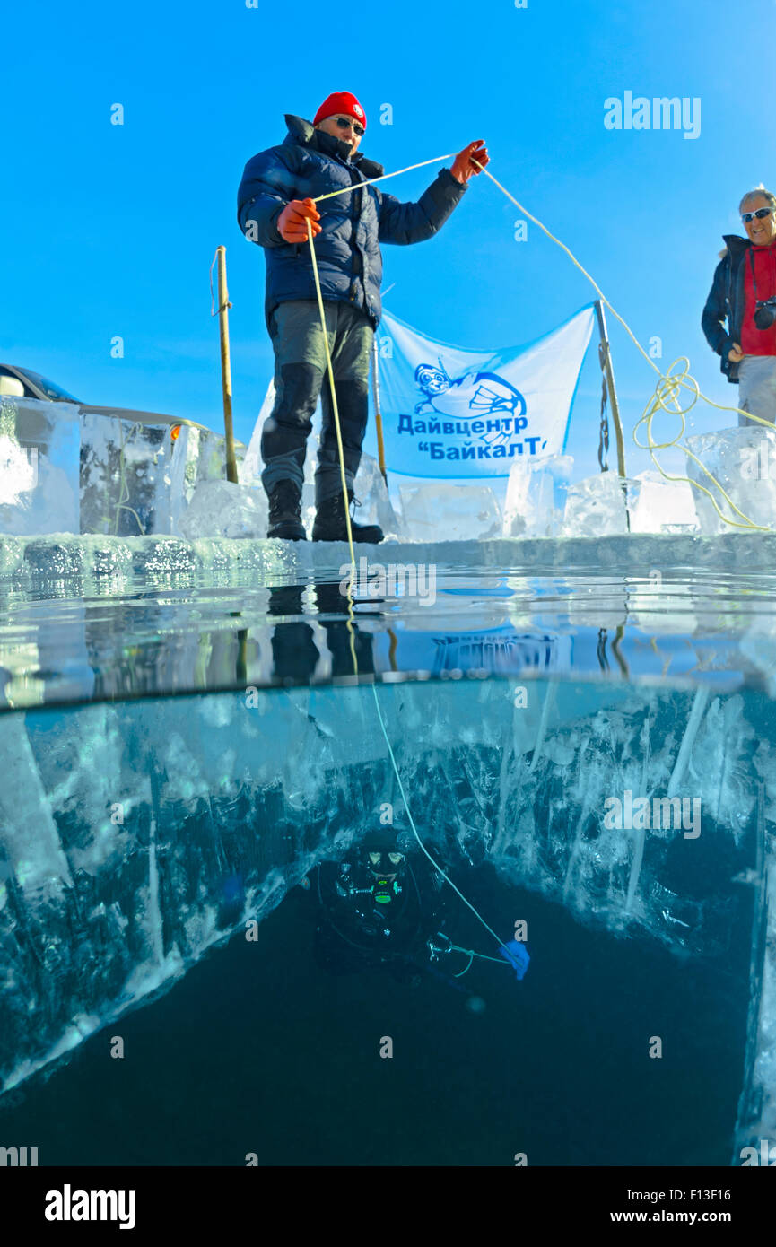 Il team di supporto sulla superficie del ghiaccio aiutando subacqueo al di sotto. Lago Baikal, Russia, marzo 2013. Foto Stock
