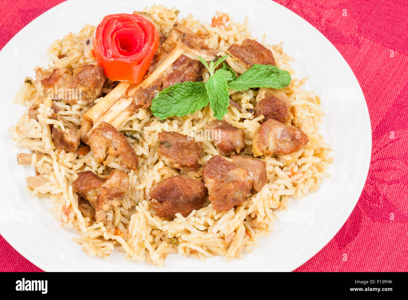 Primo piano vista dalla cima di deliziose carni di montone (agnello) biryani guarnita con la buccia di pomodoro e le foglie di menta. Foto Stock