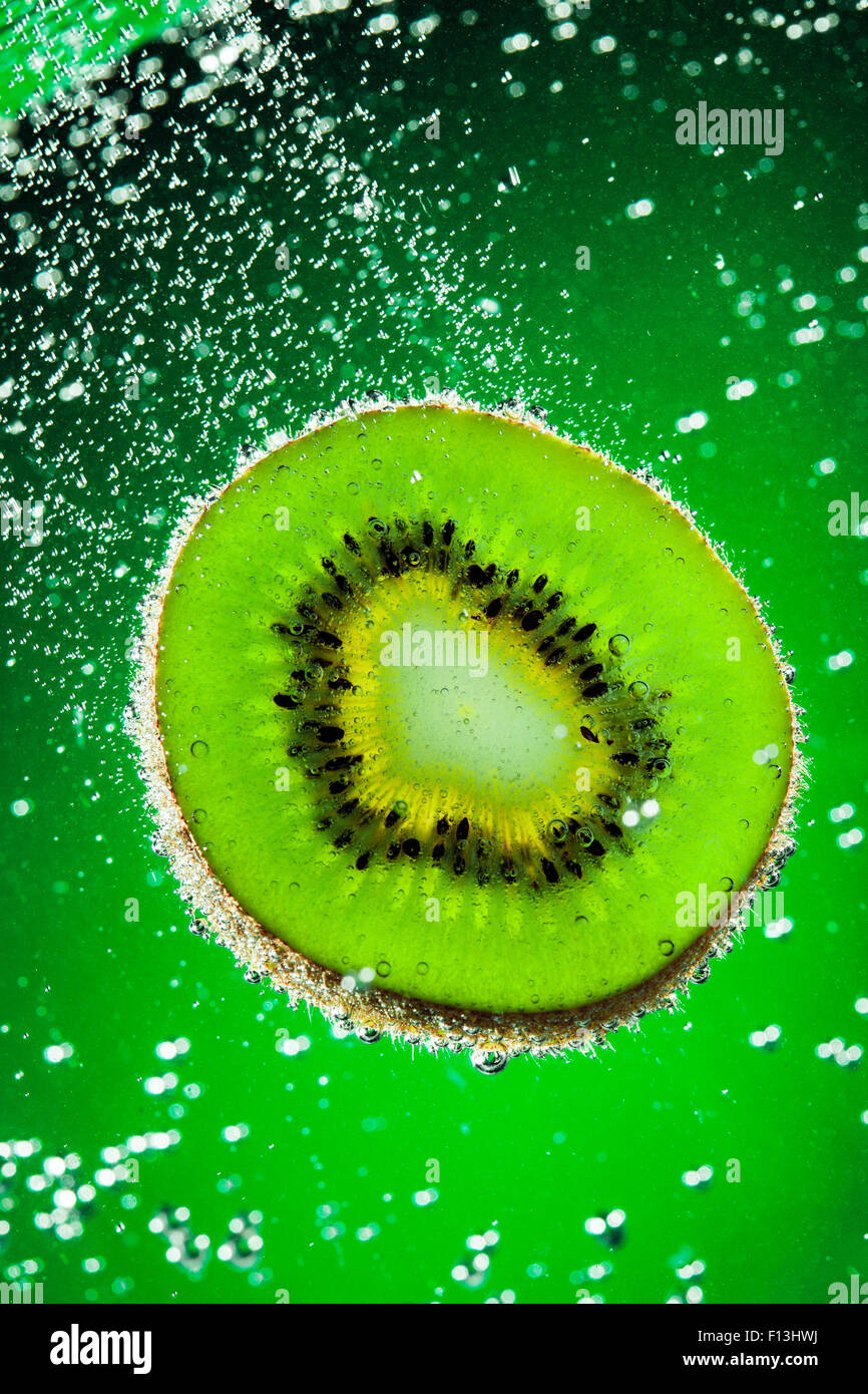 Kiwi freschi cade in acqua su uno sfondo verde Foto Stock