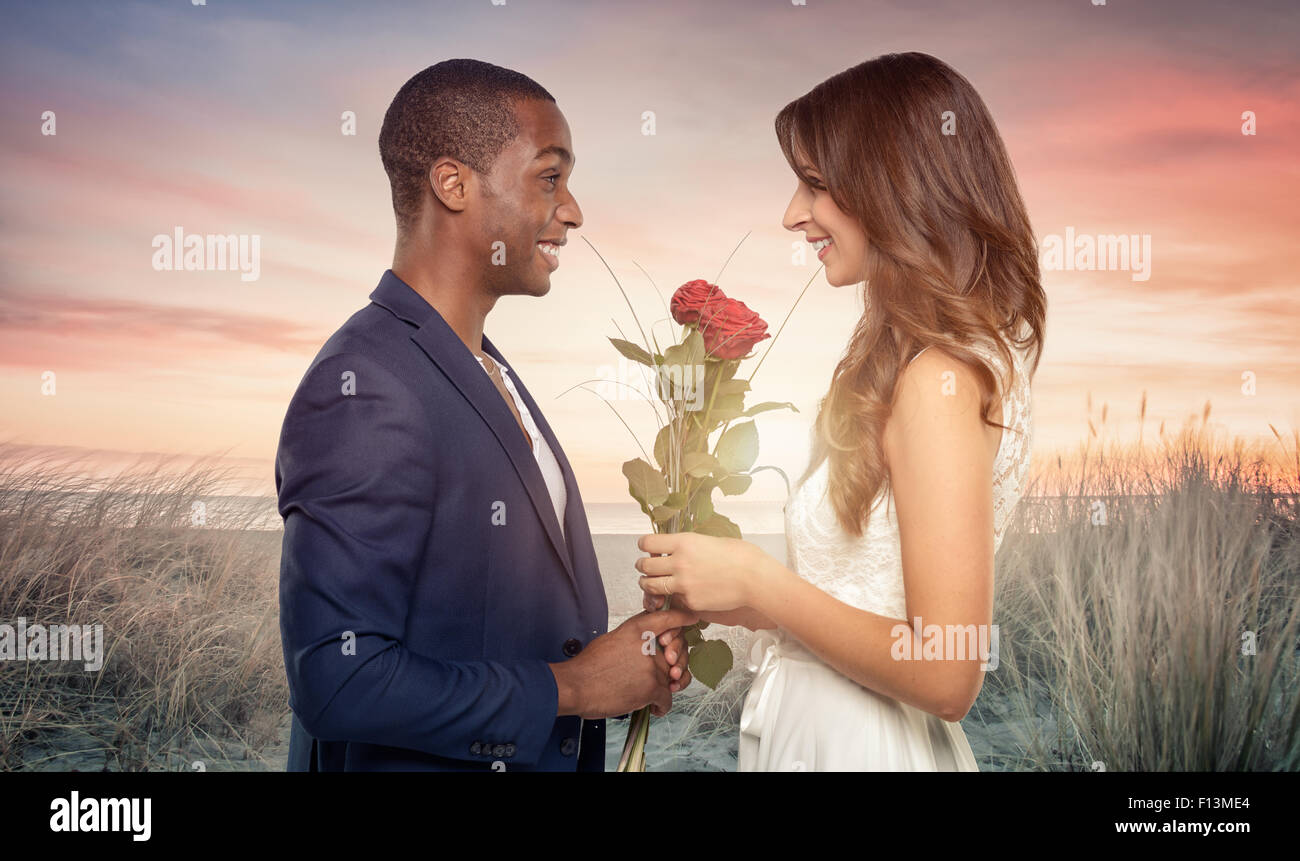 Sorridente romantico bello giovane africano propone per la sua amata come egli innesti un mazzetto di alto fusto rose rosse nella sua Foto Stock