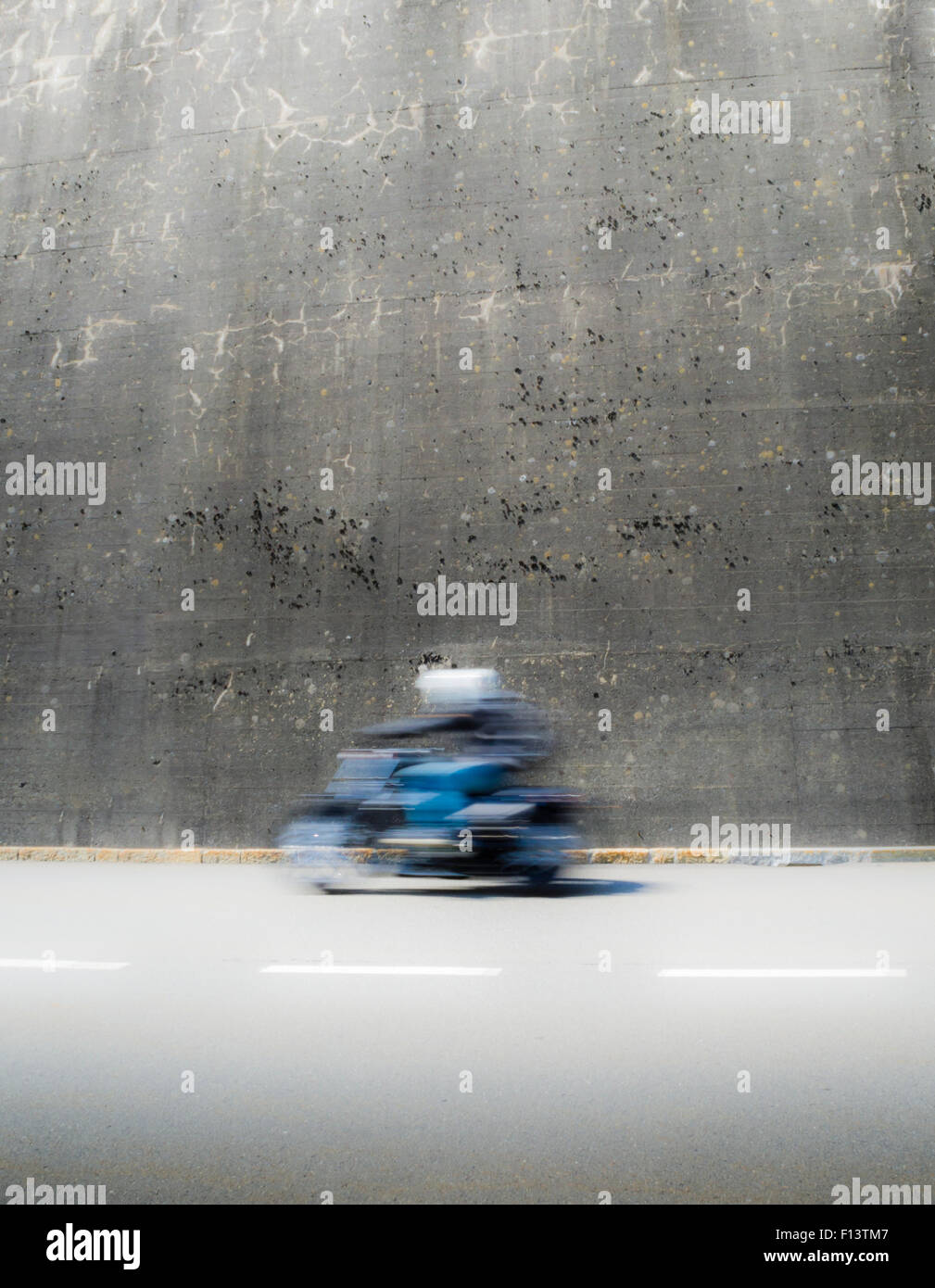 Sfocata immagine del movimento di moto rider guidando attraverso un muro di cemento. Foto Stock