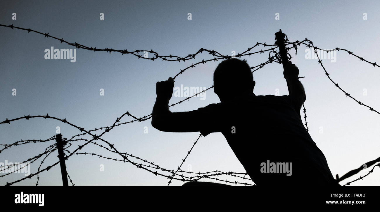 Uomo che guarda attraverso il filo spinato al tramonto. Modello rilasciato border crossing/immigrazione clandestina/rifugiato... concetto di immagine. Foto Stock