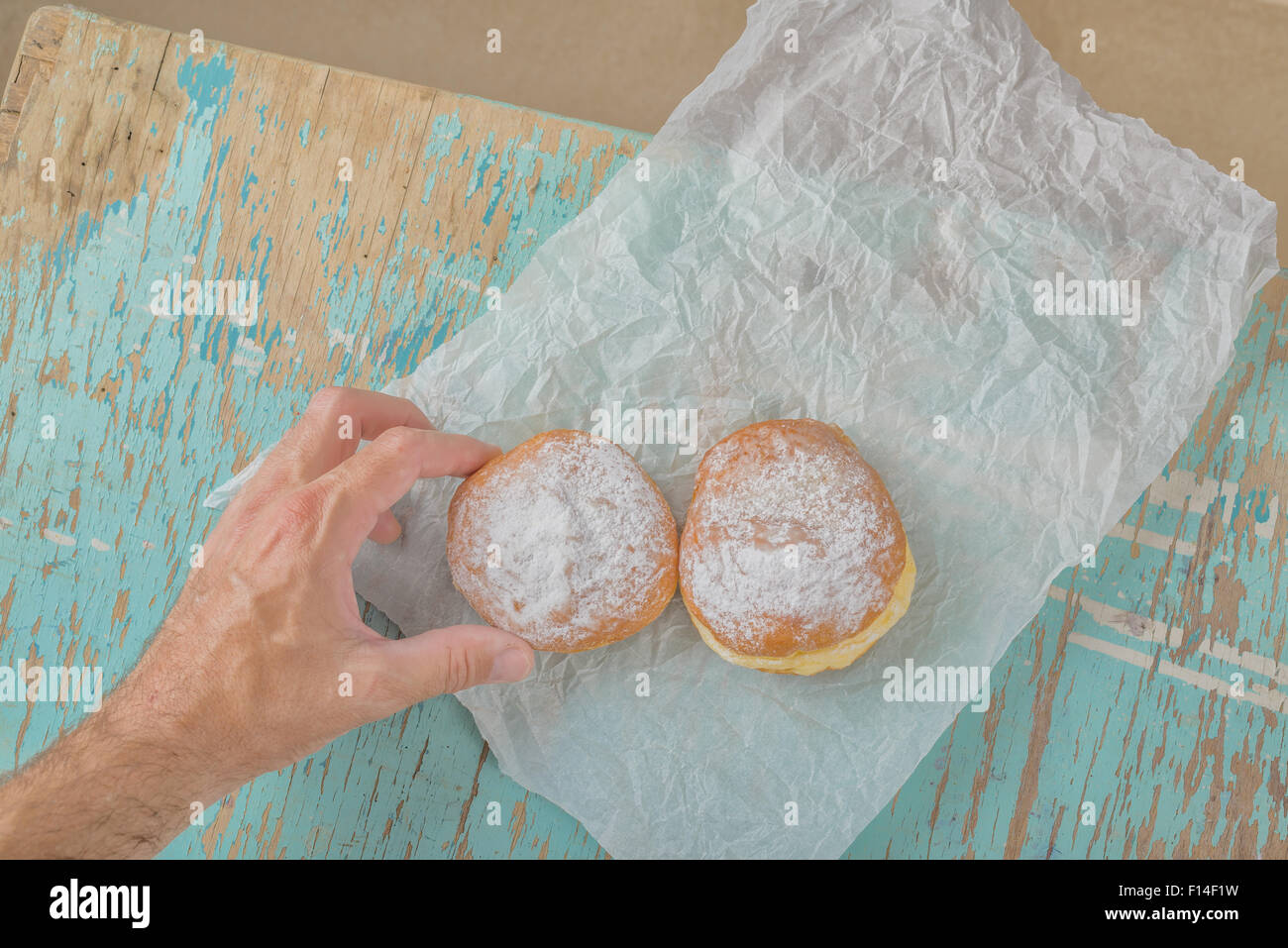 Maschio raggiunge la mano e tenendo il dolce zuccherino di donut da legno rustico tavolo da cucina, forno gustose ciambelle overhead shot, vista dall'alto Foto Stock
