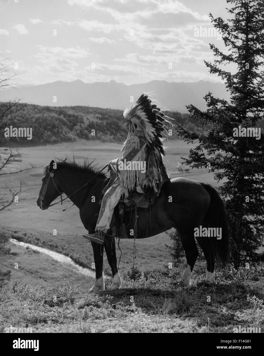 1920s NATIVE AMERICAN STONEY SIOUX UOMO PIENO EAGLE FEATHER COPRICAPO A CAVALLO guardando sopra la valle di Alberta in Canada Foto Stock