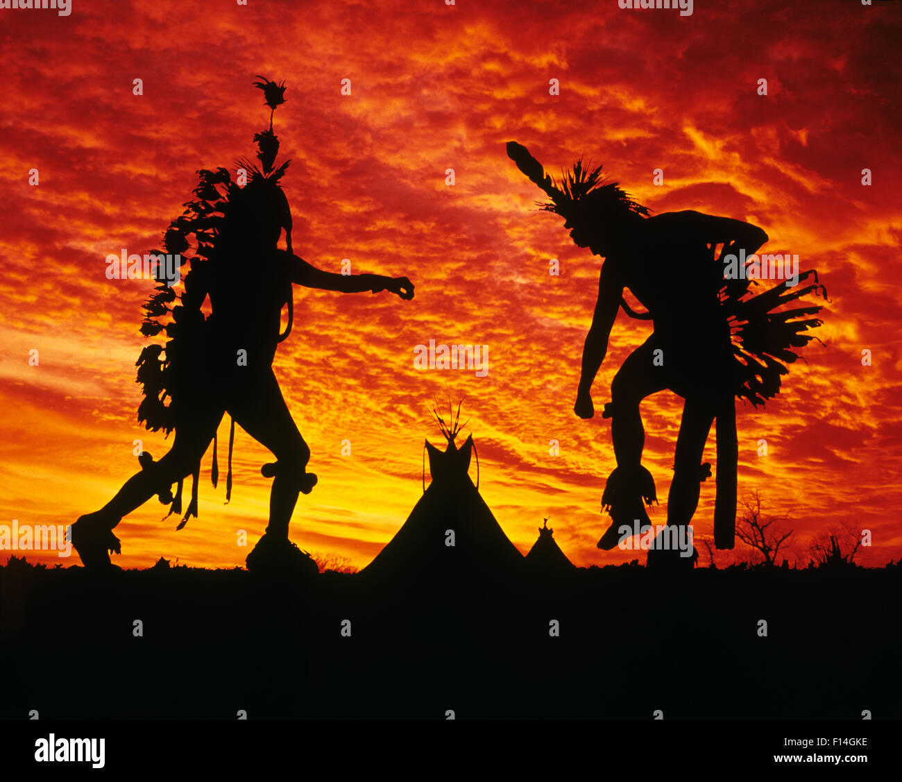 All'alba o al tramonto silhouette di due nativi indiani americani uomini DANCING AT POW WOW CON TEPEES IN BACKGROUND Foto Stock