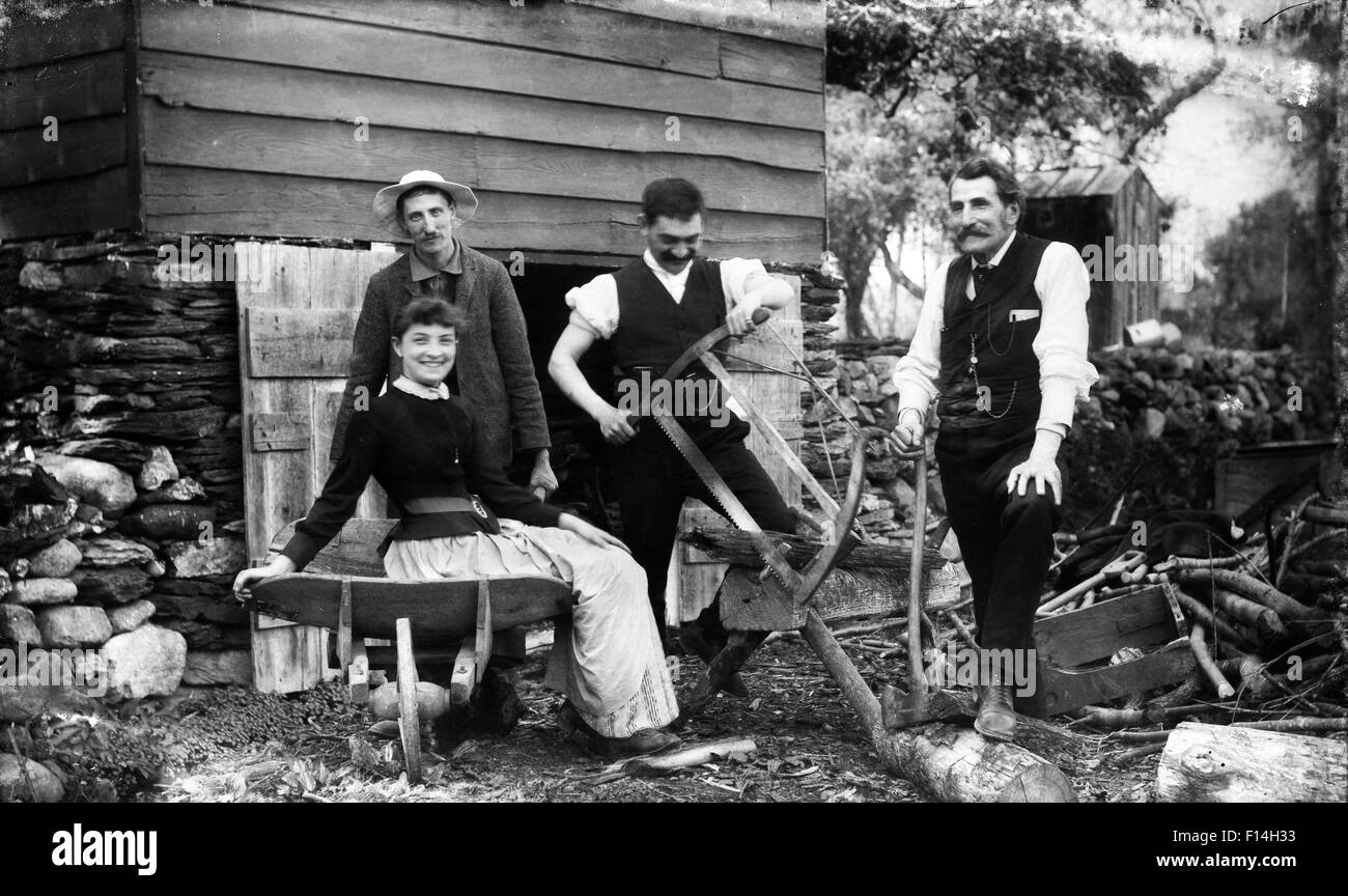 1890s tre uomini una donna di casa capannone guardando la fotocamera di un solo uomo il taglio di legna da ardere tronchi con sega a telaio Foto Stock