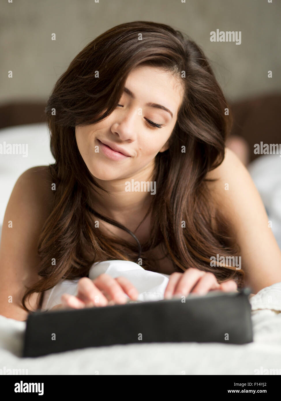 La donna posa sul letto tramite tavoletta digitale Foto Stock
