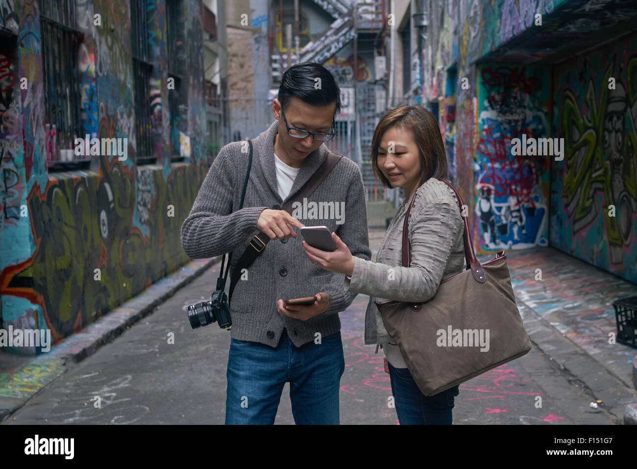 Uomo e donna che guarda al telefono con Melbourne la famosa arte di strada /graffiti arte alle pareti in background Foto Stock