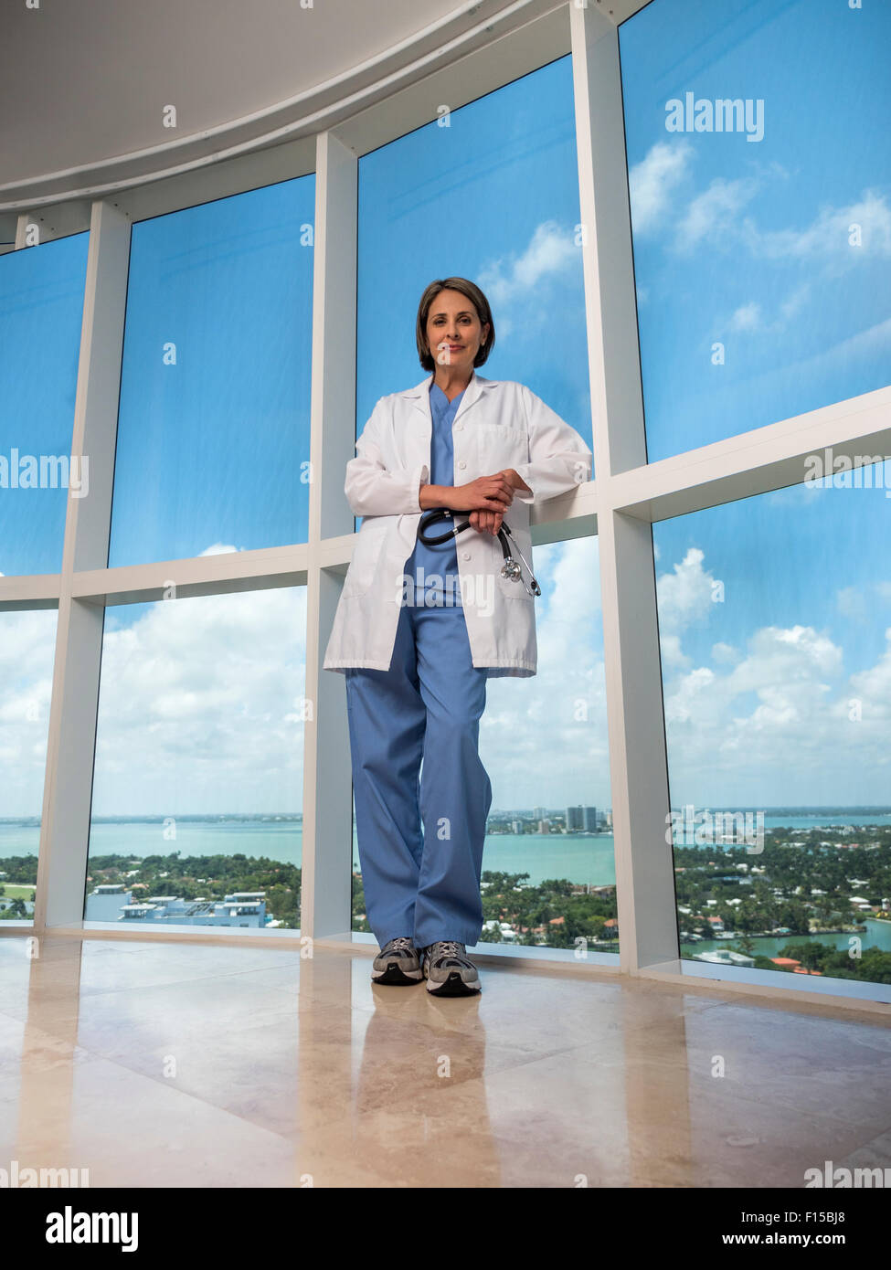 Femmina matura medico in piedi vicino alla finestra di uno stetoscopio di contenimento Foto Stock