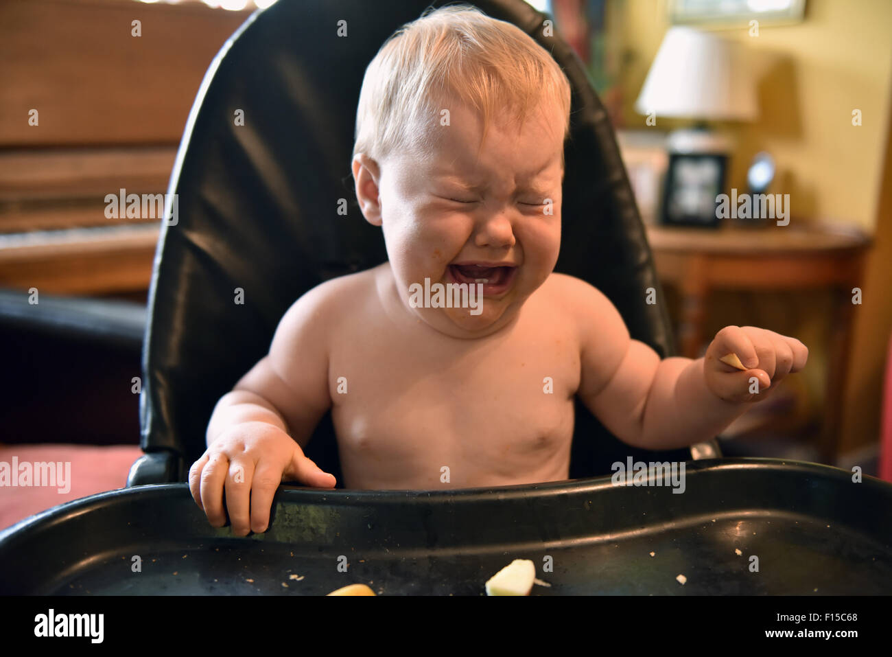 Un undici mesi con una temperatura seduto nel suo seggiolone piangere. Foto Stock