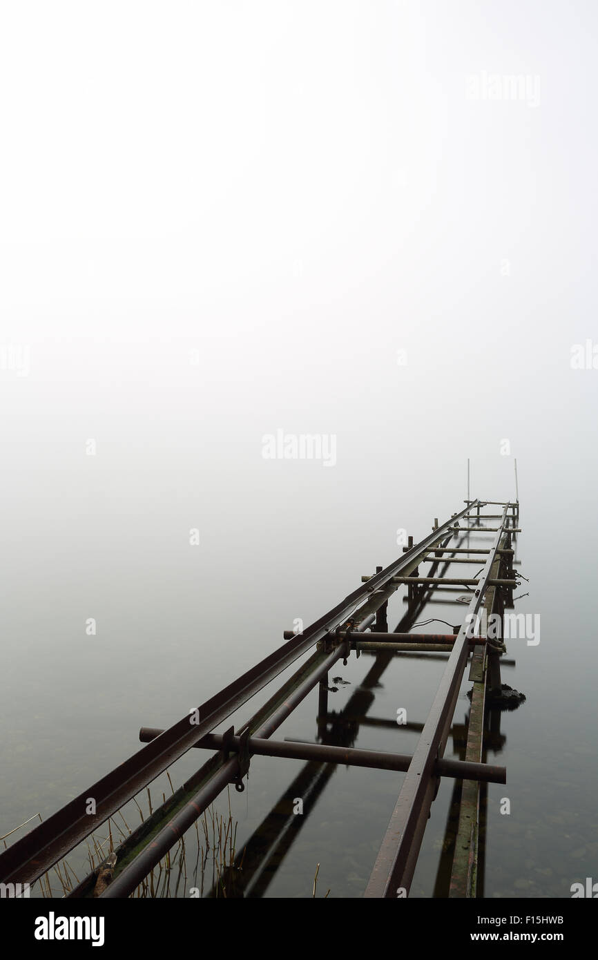 Un vecchio molo dalle sponde del Loch Lomond nella nebbia Foto Stock