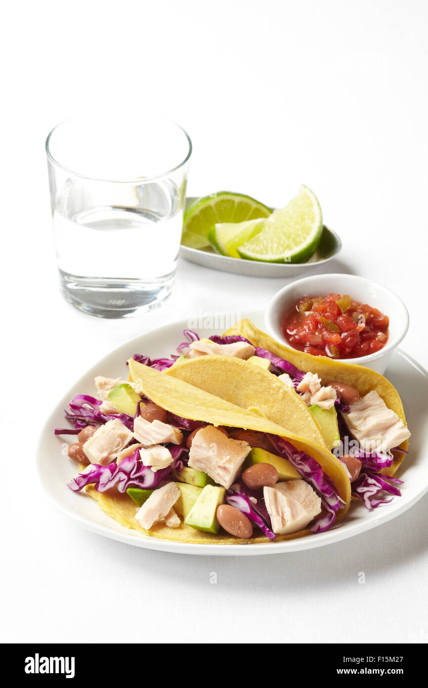 Tacos di tonno con avocado, cavolo e fagioli su piastra con salsa, tigli e un bicchiere di acqua, studio shot su sfondo bianco Foto Stock